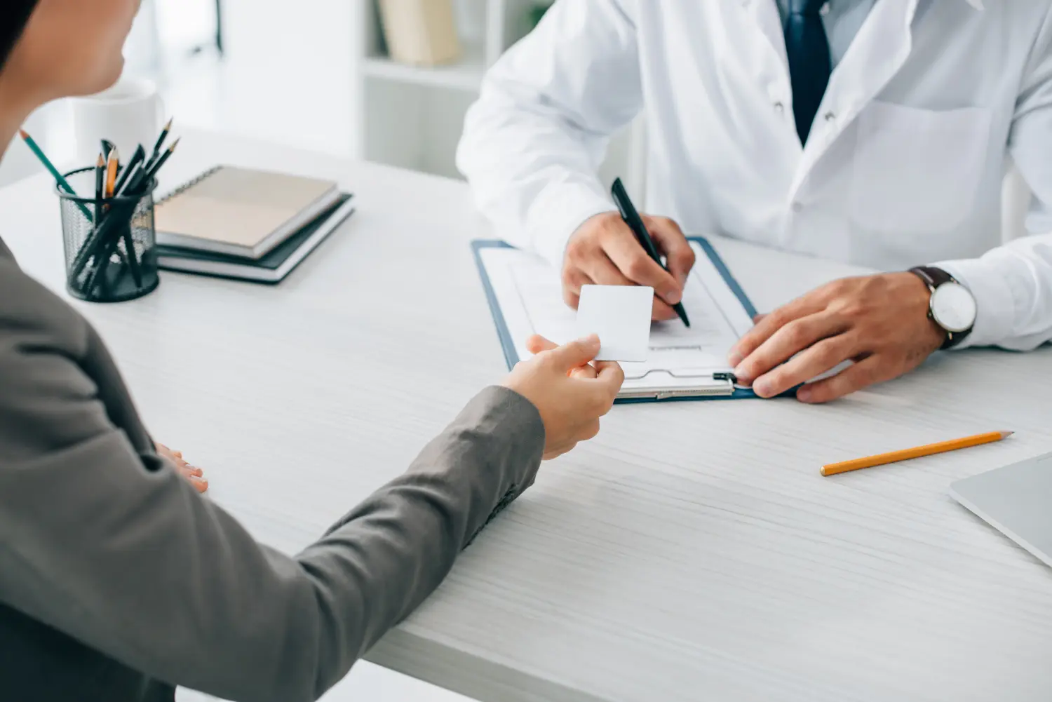 Patient überreicht einer Ärztin die Versicherungskarte zum Ausfüllen des Formulars