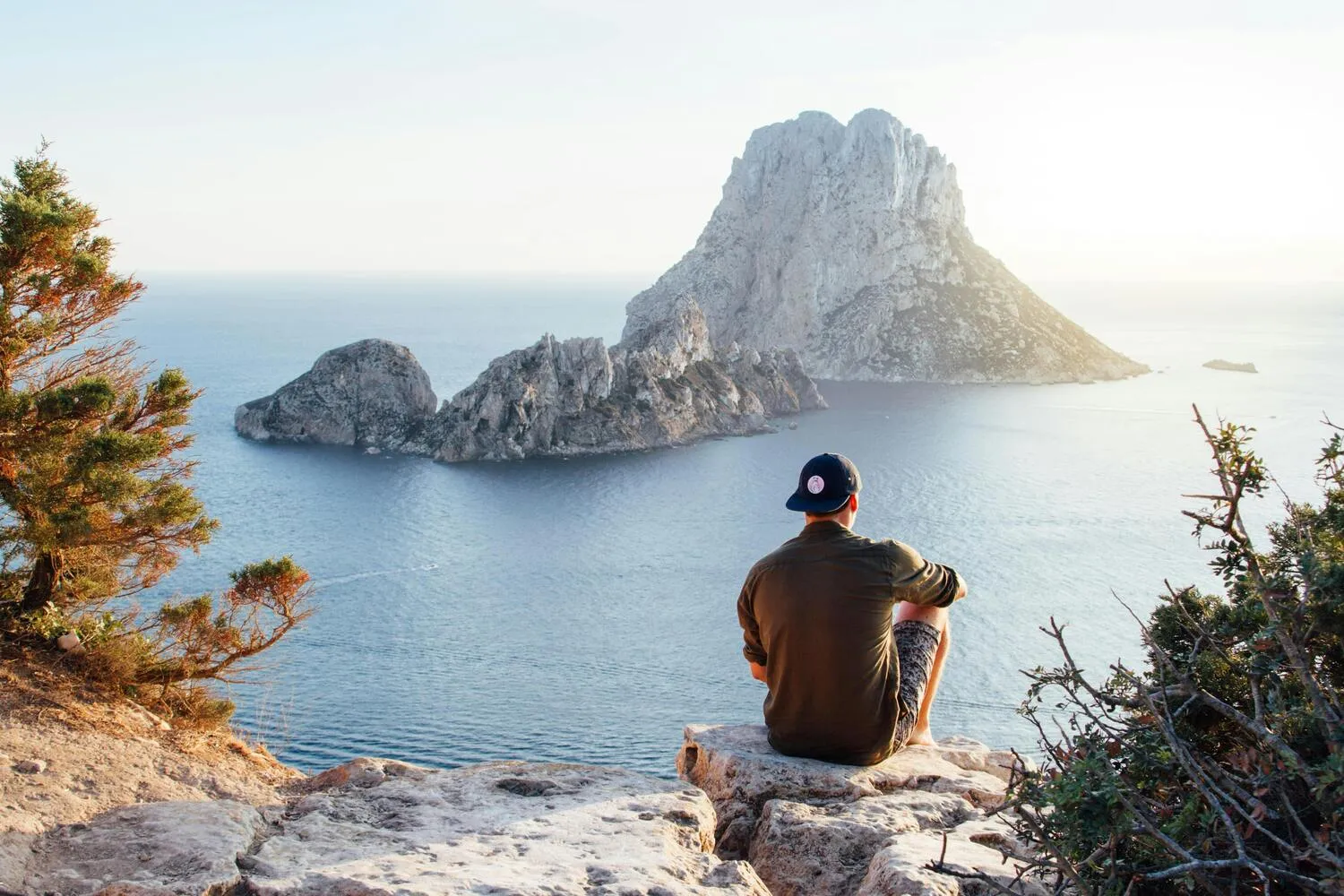 Wanderer sitzt auf einer Klippe und blickt auf das Meer
